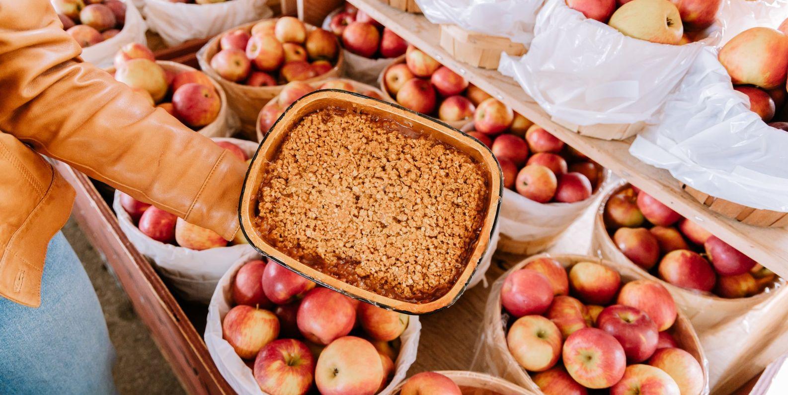 Person holding an apple pie above baskets of apples