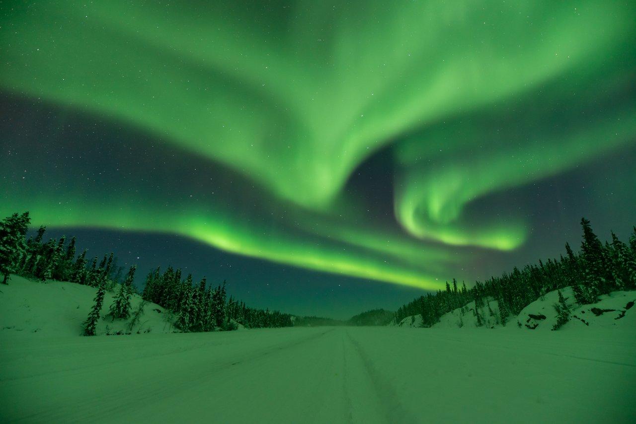 The green aurora lighting up the sky above an ice road at night.