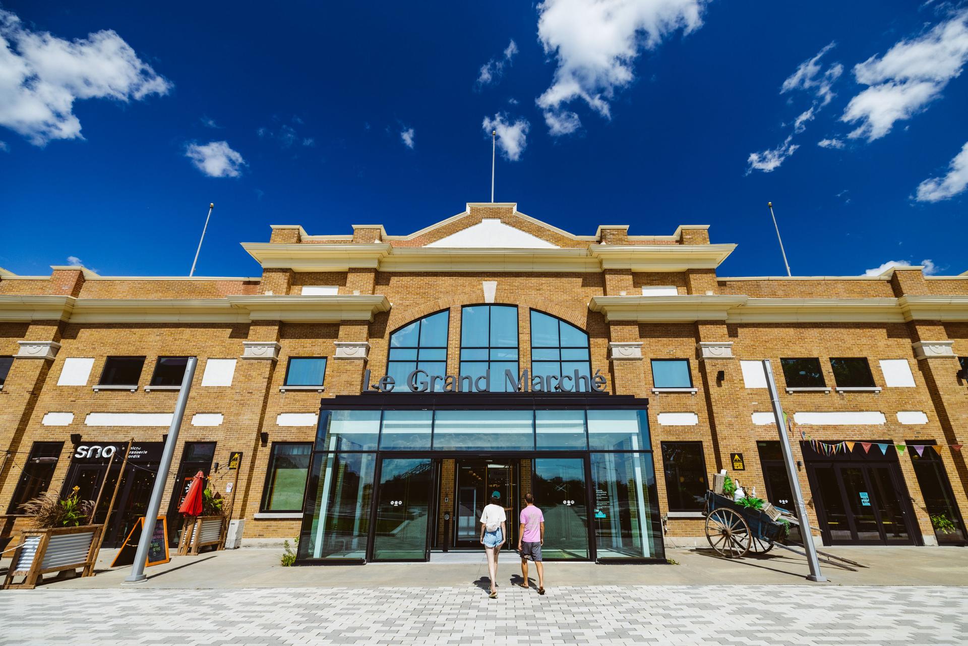 Entrance of Le Grand Marché, a brick marketplace under a bright blue sky