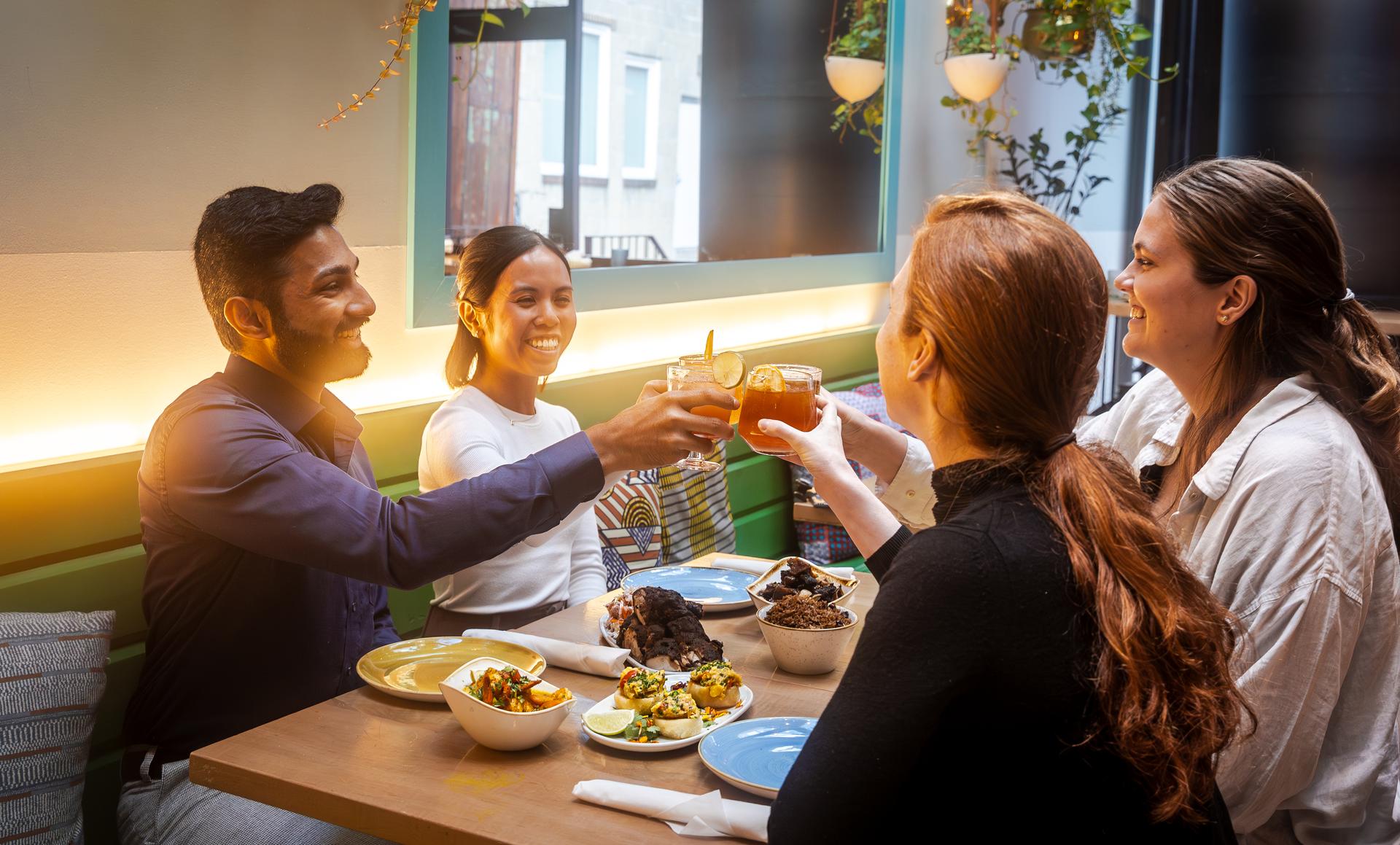 Four people raising a toast at a table with plates of food in Chubby's Jamaican Kitchen, Toronto.
