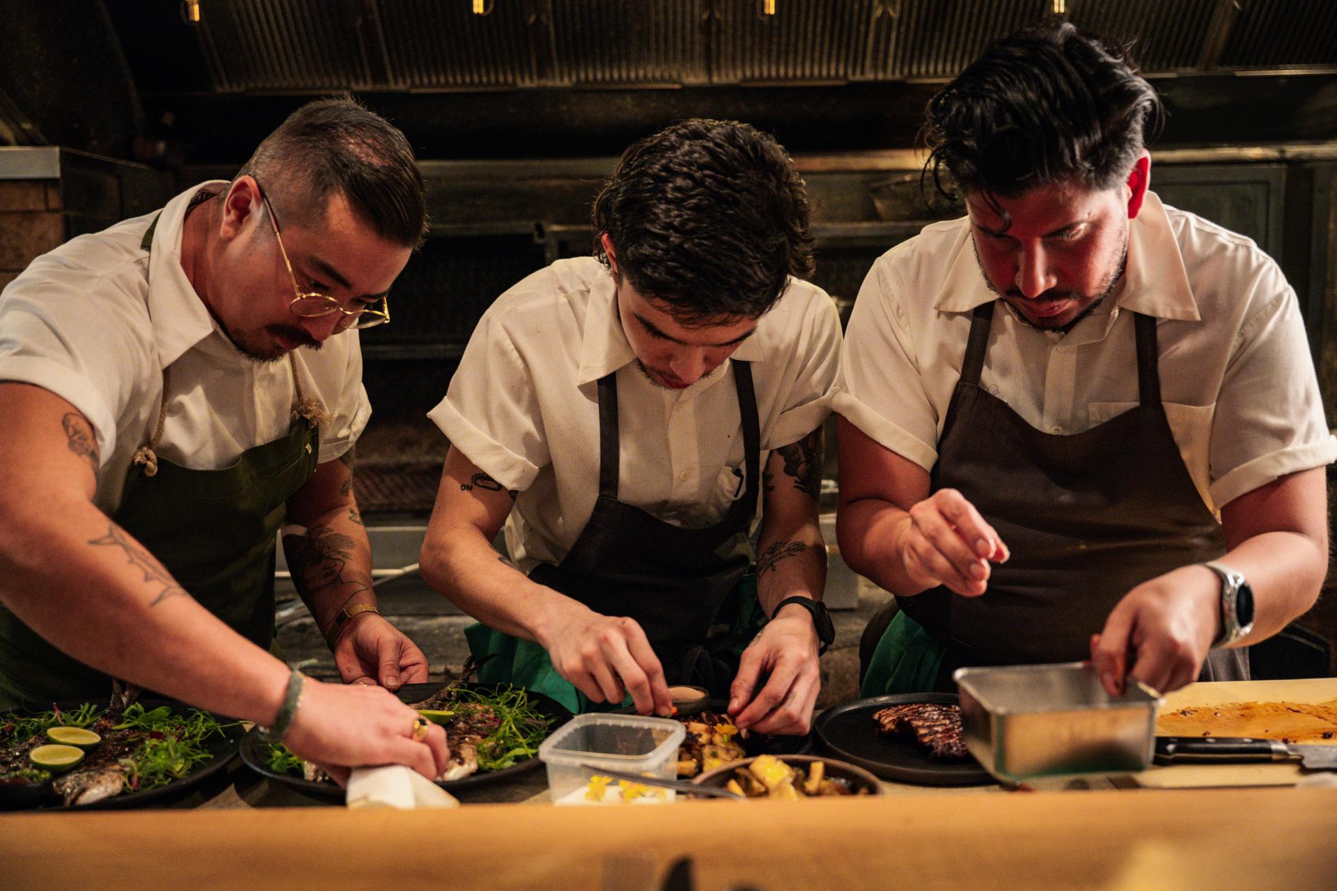 Three chefs working on plating food at a fine dining restaurant.
