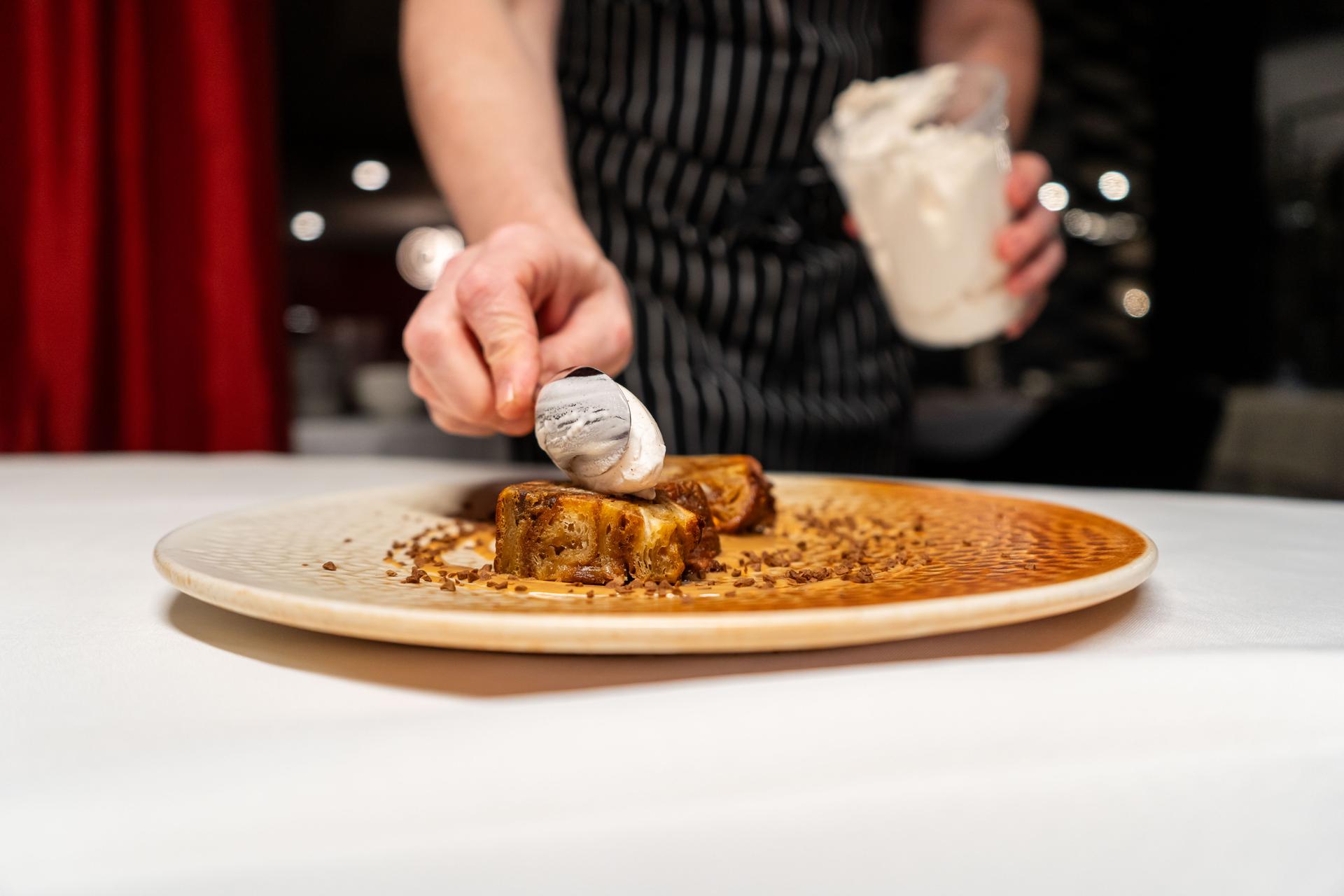 A closeup shot of a person placing a scoop of ice cream on a dessert at a fine-dining restaurant.