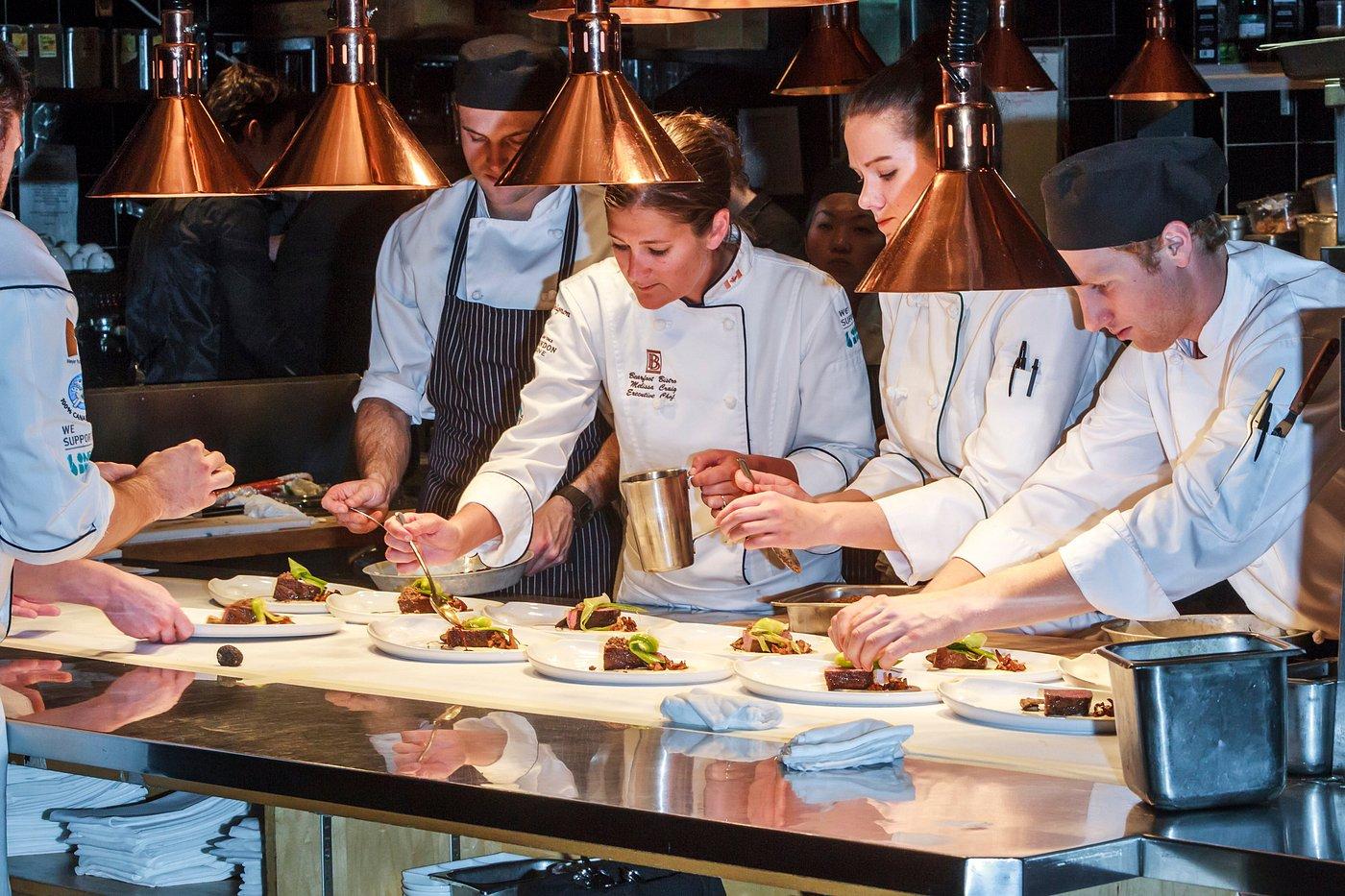 A group of chefs plating food in the kitchen of a fine dining restaurant.