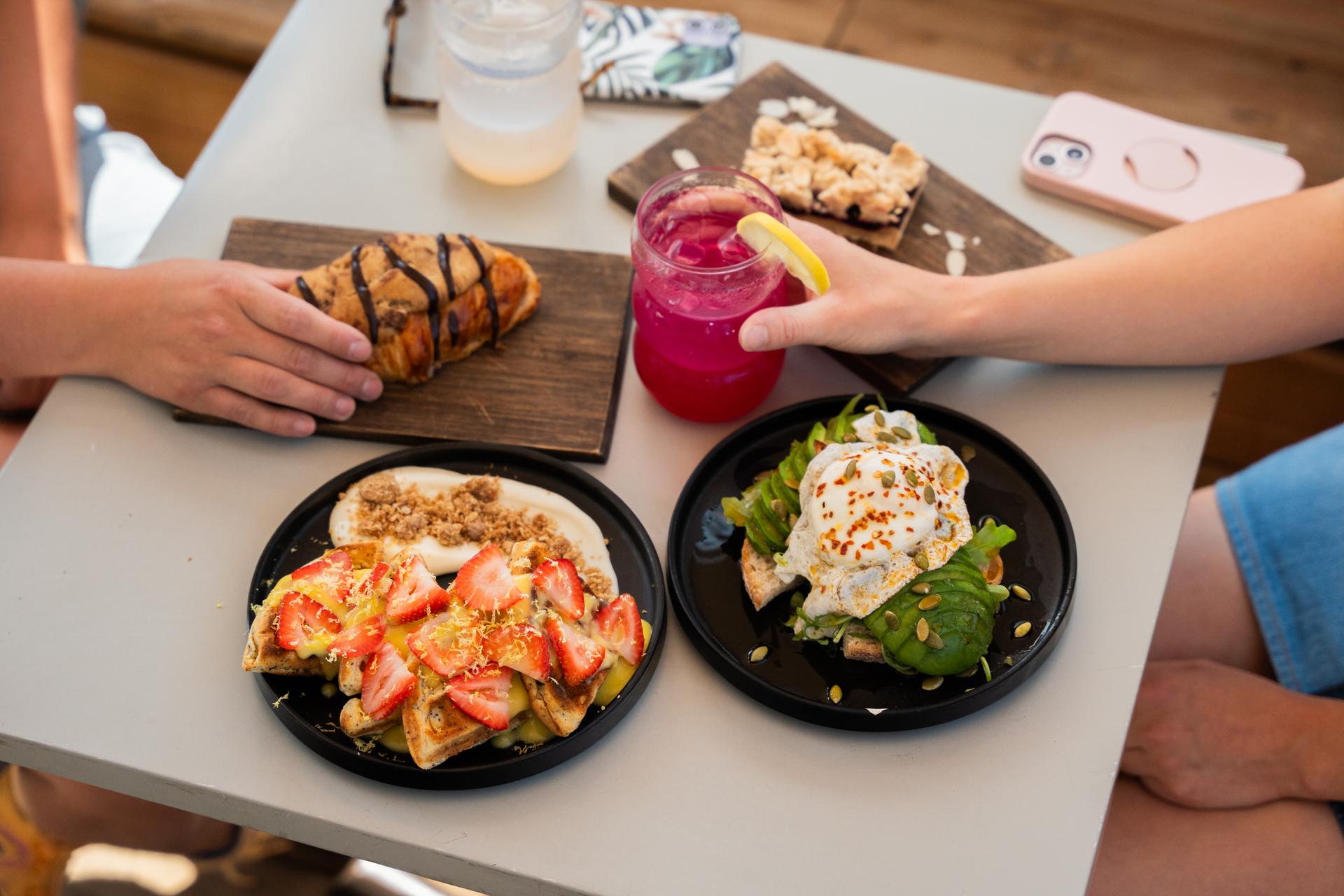 A table with a variety of brunch items, including a chocolate-drizzled pastry, a fruit crumble bar, a plate of waffles