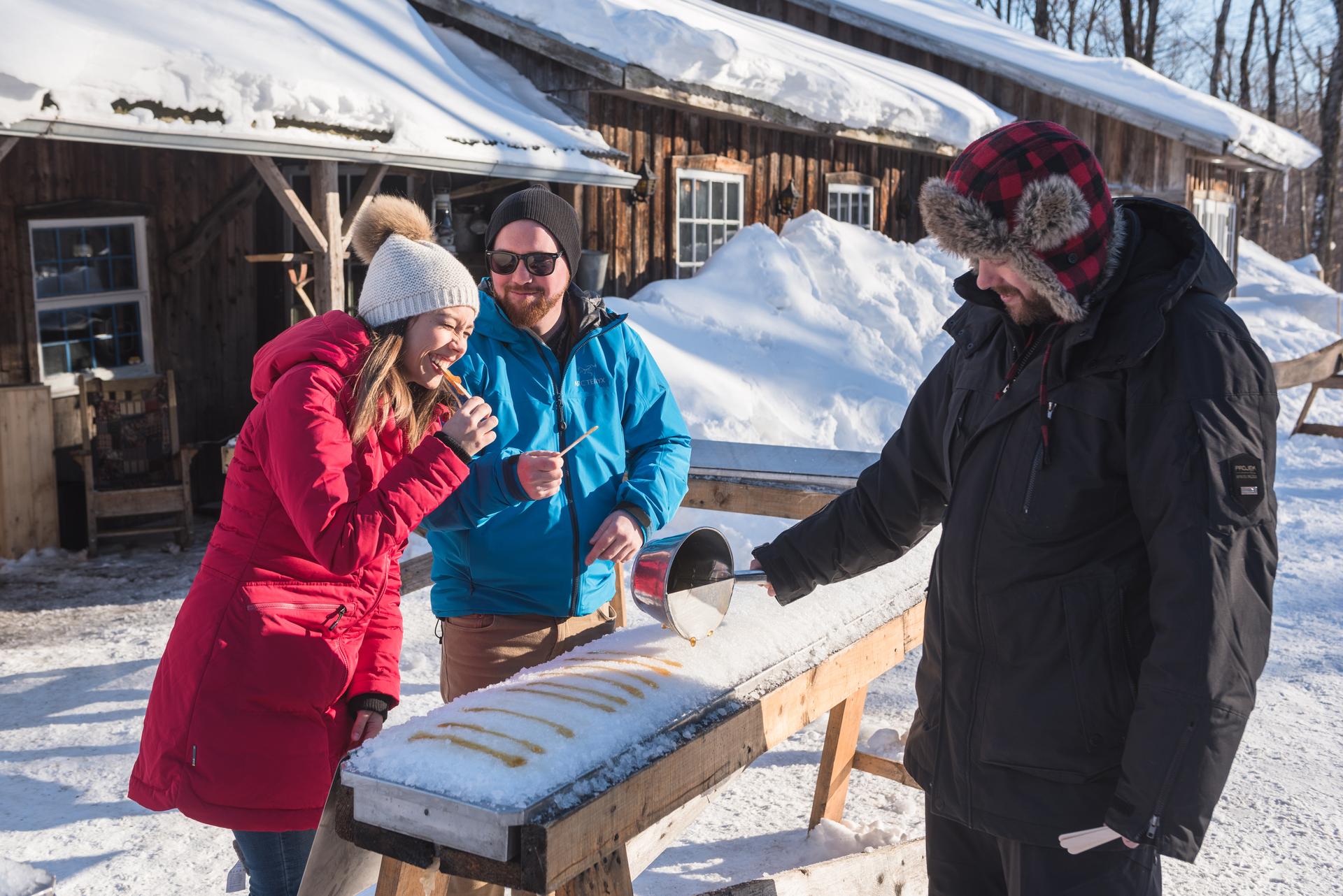 People enjoying maple taffy on snow at a rustic outdoor setting.