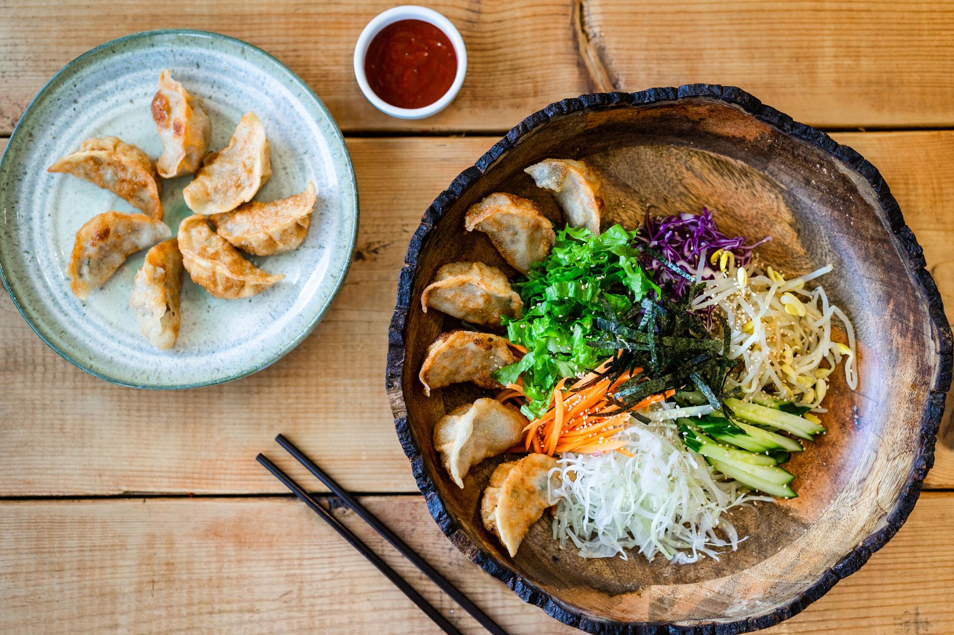 A wooden bowl filled with dumplings and colorful fresh vegetables