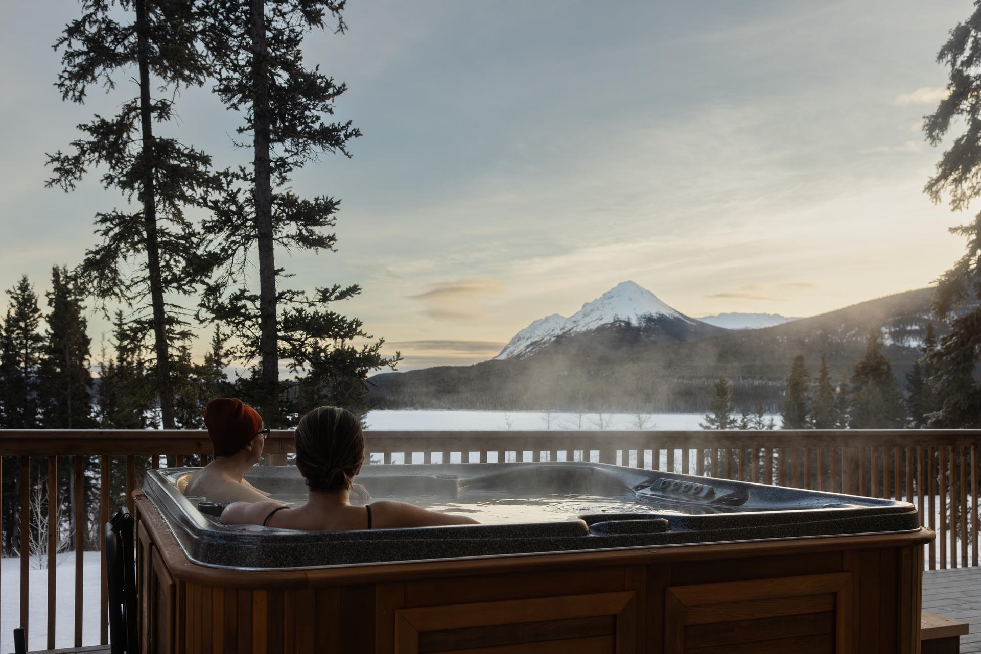 A couple sitting in a steaming hot tub facing mountain views