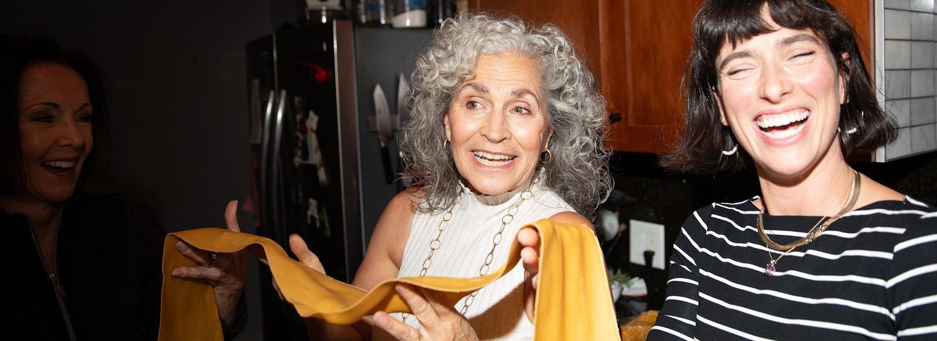 Two people smiling and holding a long piece of pasta