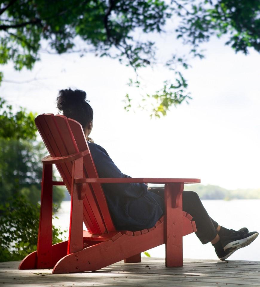A person sitting on a red chair and looking out at the water