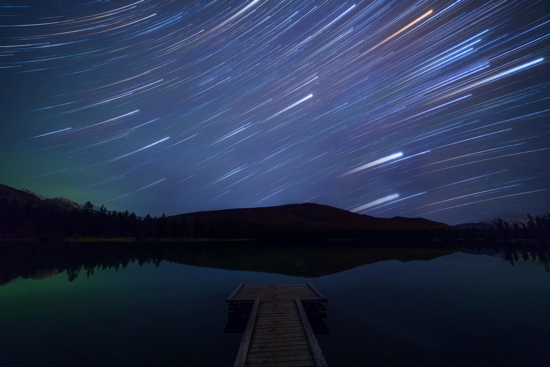 Star trails streak across the night sky above a quiet lake and dock