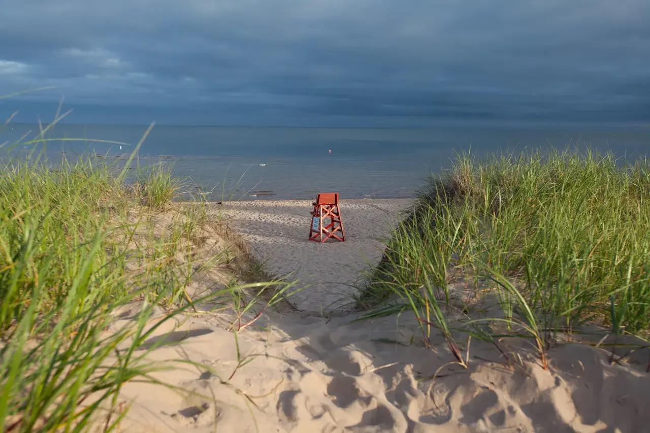 A lifeguard chair stands on Basin Head’s famous singing sands with dune grasses framing warm, shallow Atlantic waters—capturing the family-friendly character of Prince Edward Island’s squeaky-soft beach where silica sand creates its distinctive sound underfoot.