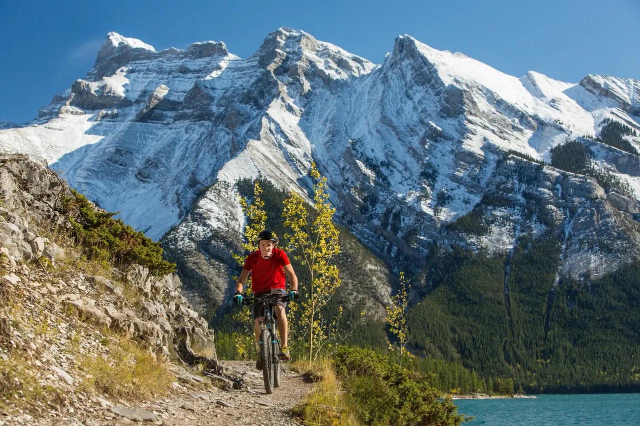 Mountain biking image supports the article’s ‘active adventure’ segment, clarifying that Rockies experiences aren’t only scenic drives—there are trail networks where water and valley corridors shape the ride routes.