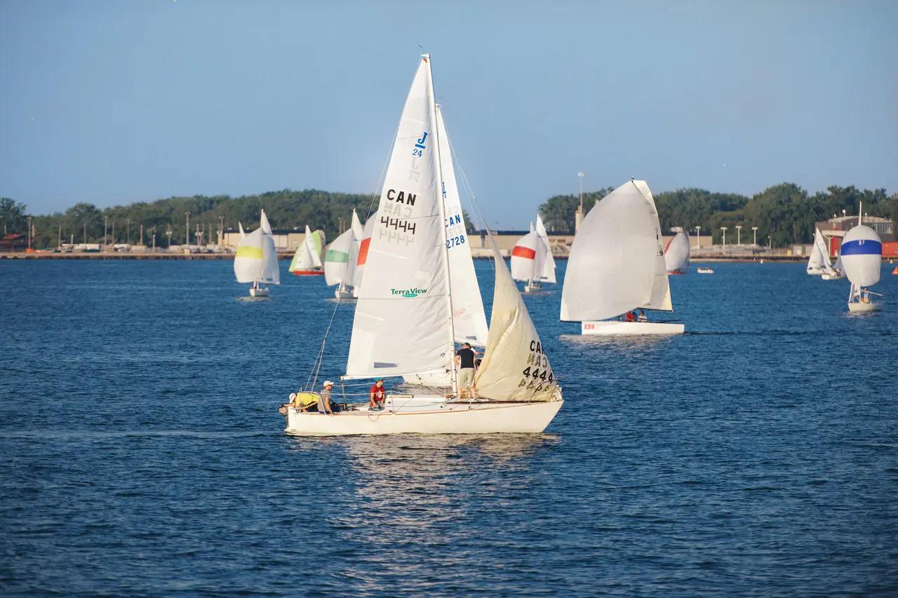 Sailboats with Canadian insignia race across Lake Ontario's blue waters near Toronto's waterfront, showcasing the recreational sailing culture on one of the world's longest urban waterfronts.