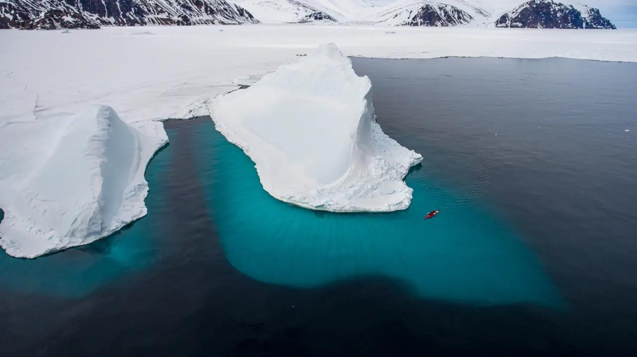 A red kayak weaving between icebergs in Nunavut, establishing that the article’s ‘kayaking and canoeing’ ideas are expedition-grade Arctic experiences, not casual day rentals.
