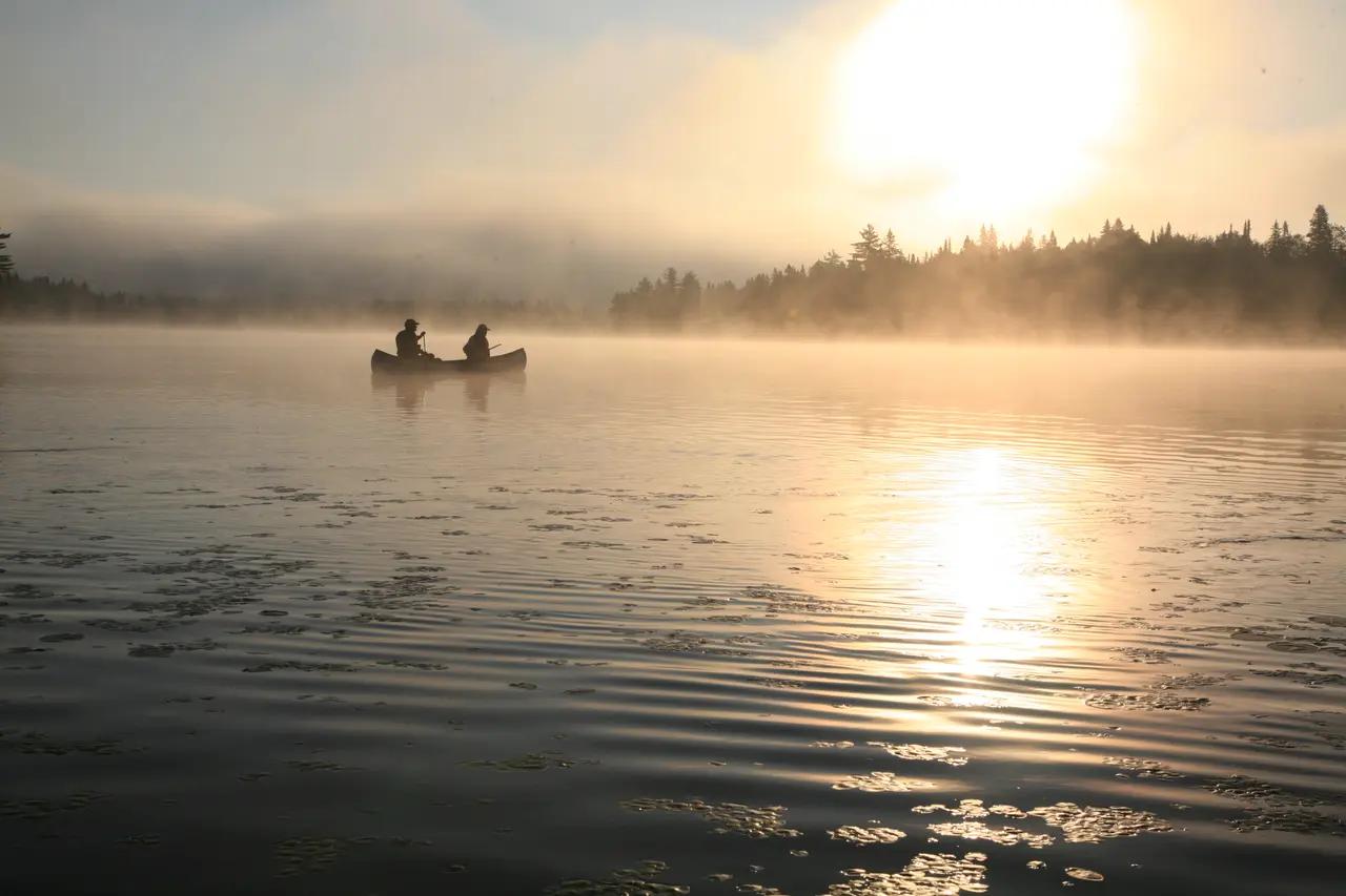 A solo canoe on a foggy Québec lake at sunrise, setting expectations for the quiet, wilderness-first canoe‑camping experiences this article recommends.