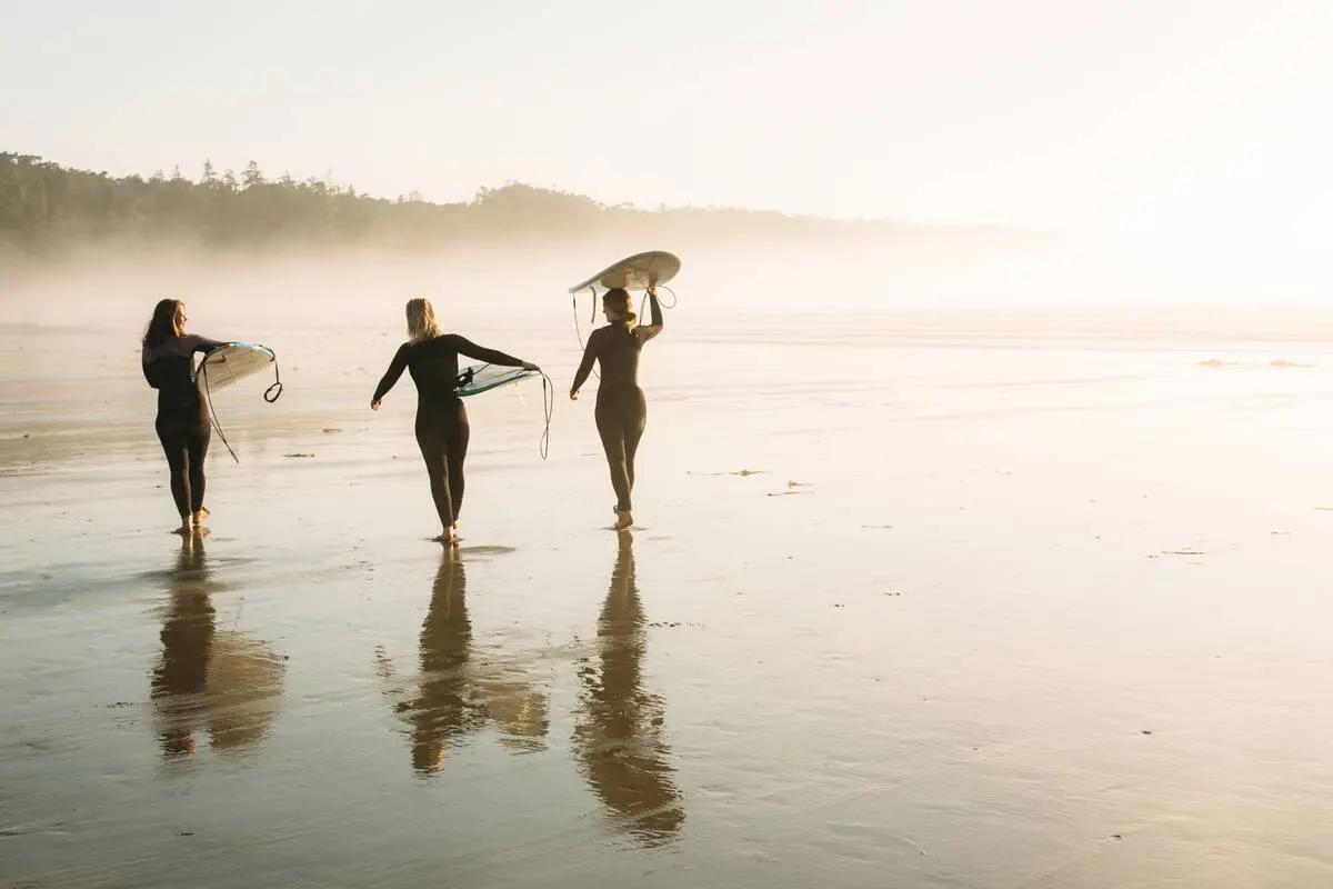 Three surfers in full wetsuits walk along Tofino’s beach at sunset with their boards, embodying the cold-water surf culture that makes Pacific Rim a year-round destination for wave riders willing to embrace the elements.