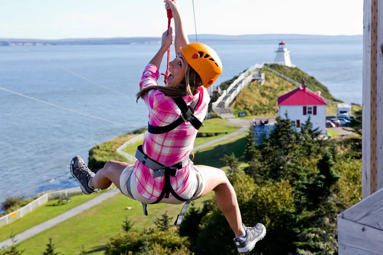 A zipliner over Cape Enrage’s coastline with the lighthouse in view, illustrating the article’s ‘edge-of-the-ocean’ adventure theme and the type of coastal viewpoints available beyond beaches.