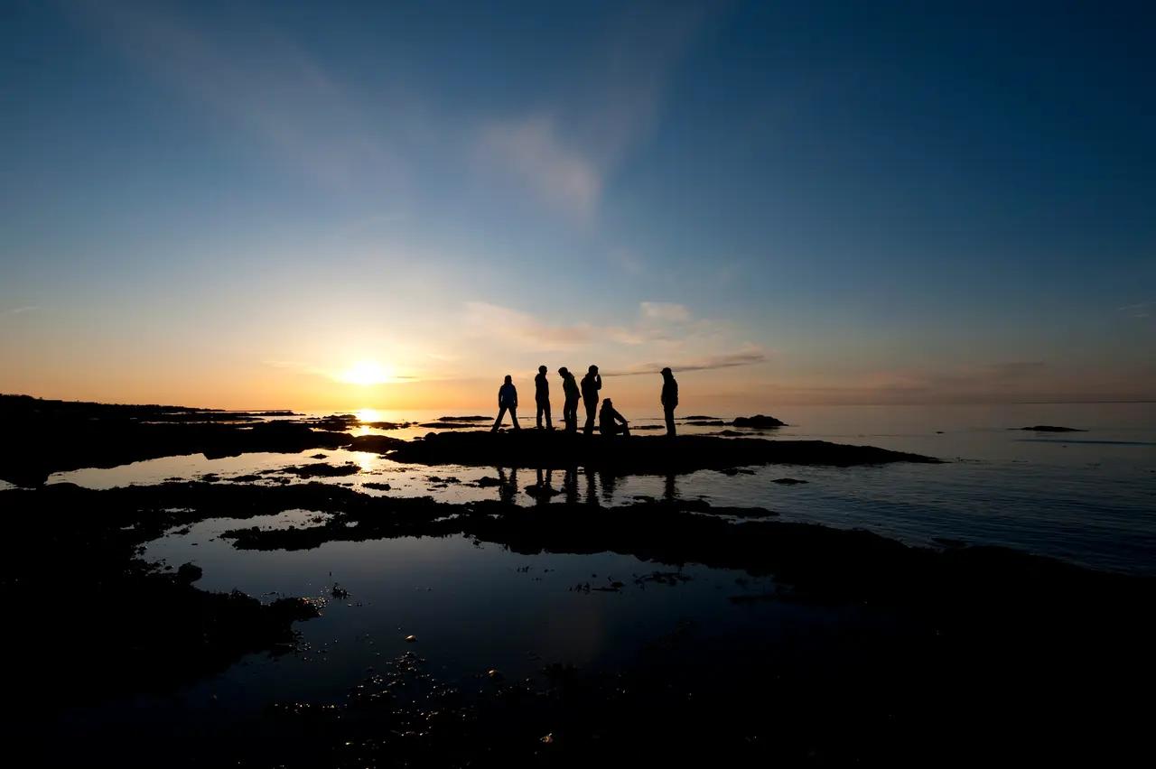 Silhouettes of visitors watching sunset from a coastal viewpoint on Quebec's Gaspé Peninsula, with golden light reflecting off the Gulf of St. Lawrence—a National Geographic top travel destination known for untamed landscapes