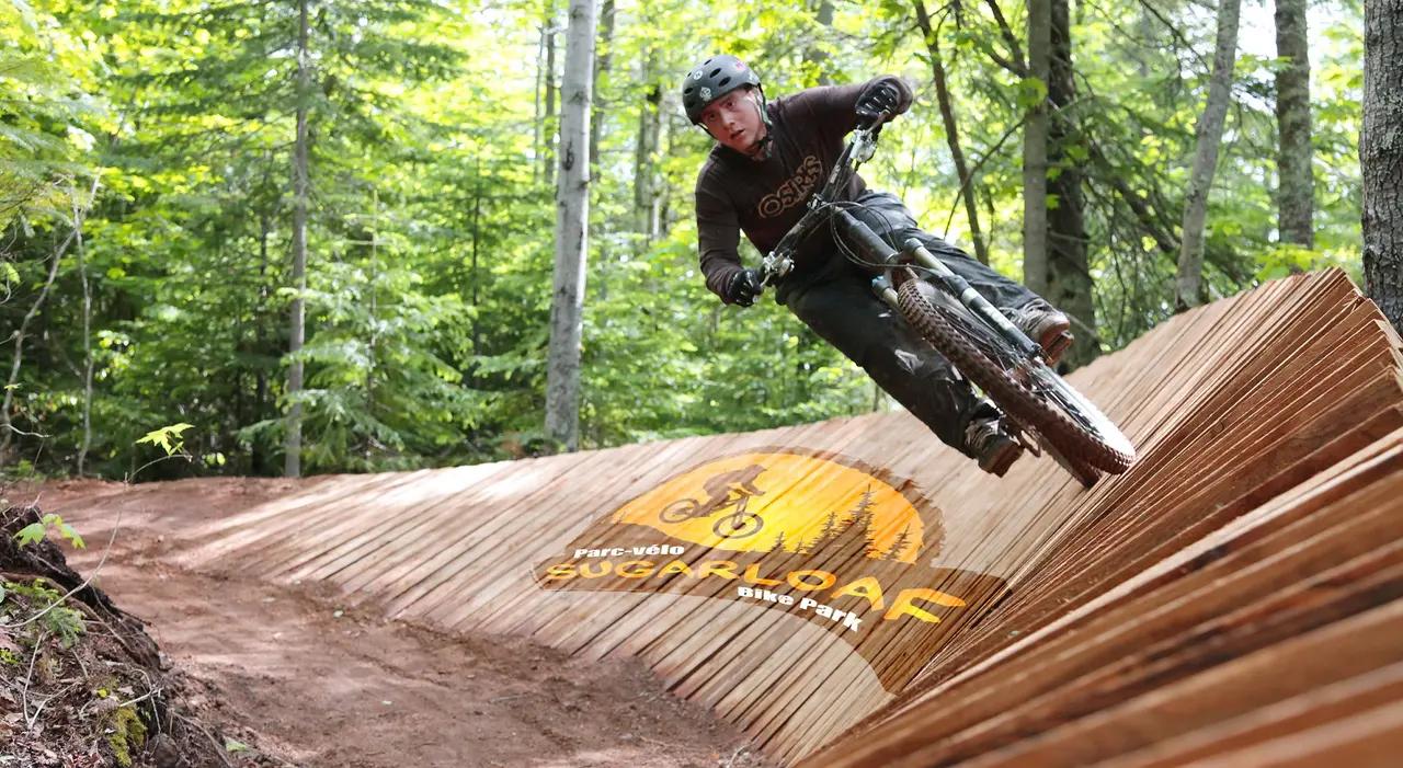 A rider banking through a built mountain-bike feature at Sugarloaf Bike Park, representing the inland adventure option in the guide and showing how New Brunswick balances coastal water experiences with land-based thrills.