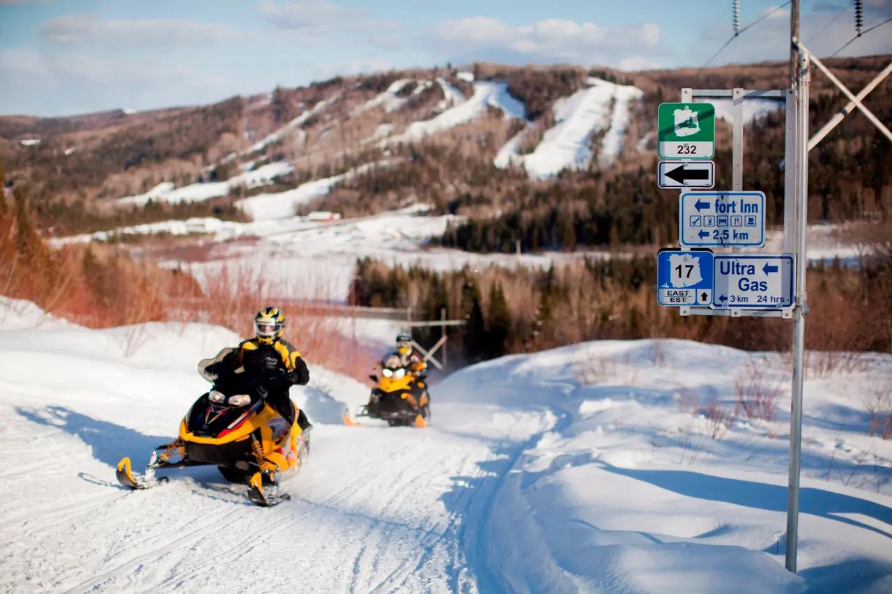 Snowmobilers riding a groomed trail in New Brunswick, representing the guide’s year-round positioning and showing that the province’s outdoor network remains accessible when water activities are seasonal.