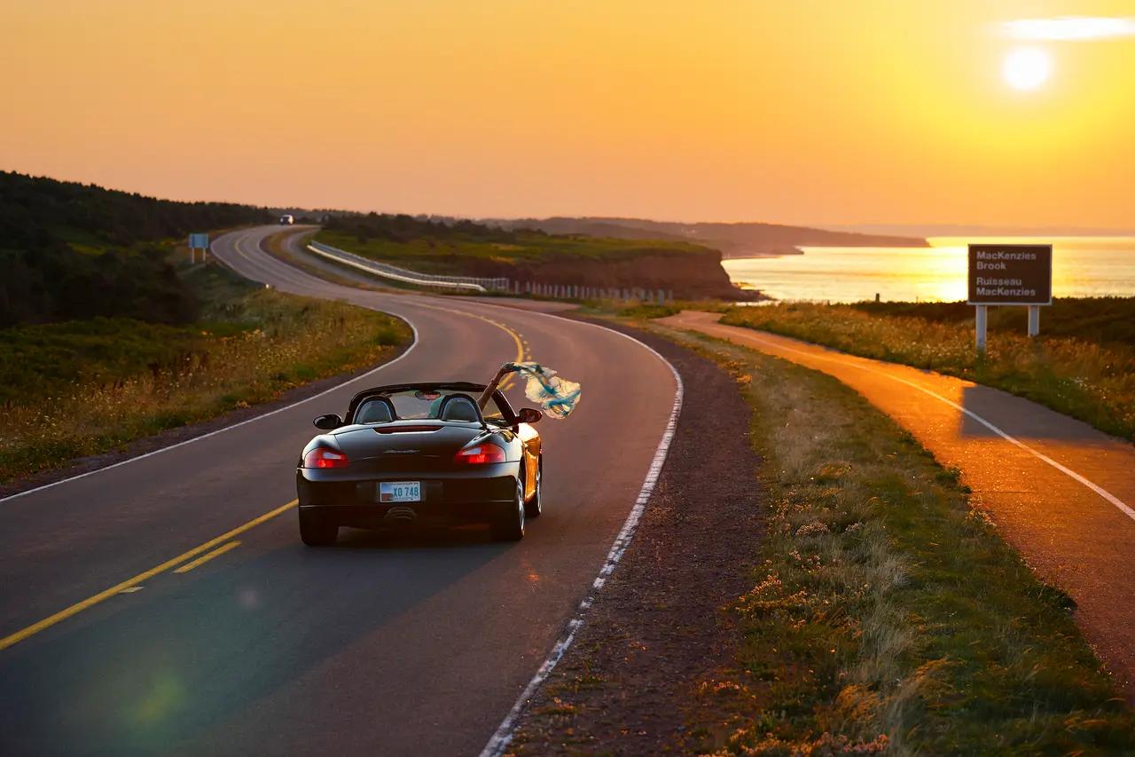 A car driving through Prince Edward Island National Park at sunset, highlighting the itinerary’s drive-time planning and the park’s role as a ‘scenic corridor’ between stops.