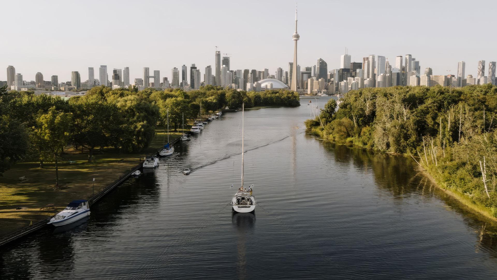Toronto skyline with sailboat on a tree-lined waterway