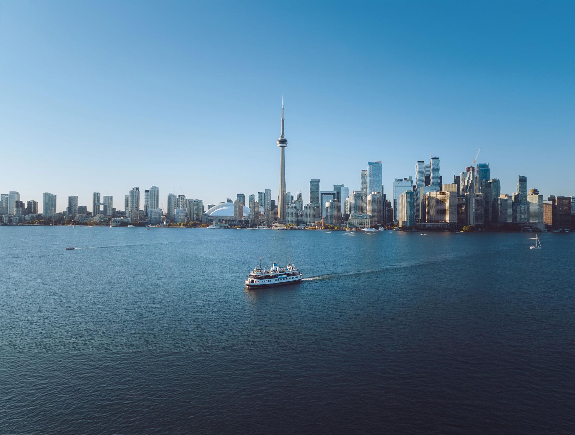 Toronto skyline viewed from the water with the CN Tower and a ferry boat under a clear blue sky