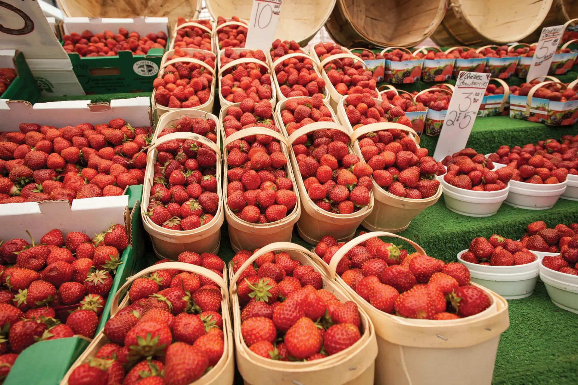 Rows of fresh strawberries packed in wooden baskets displayed at an outdoor farmer’s market on a sunny day