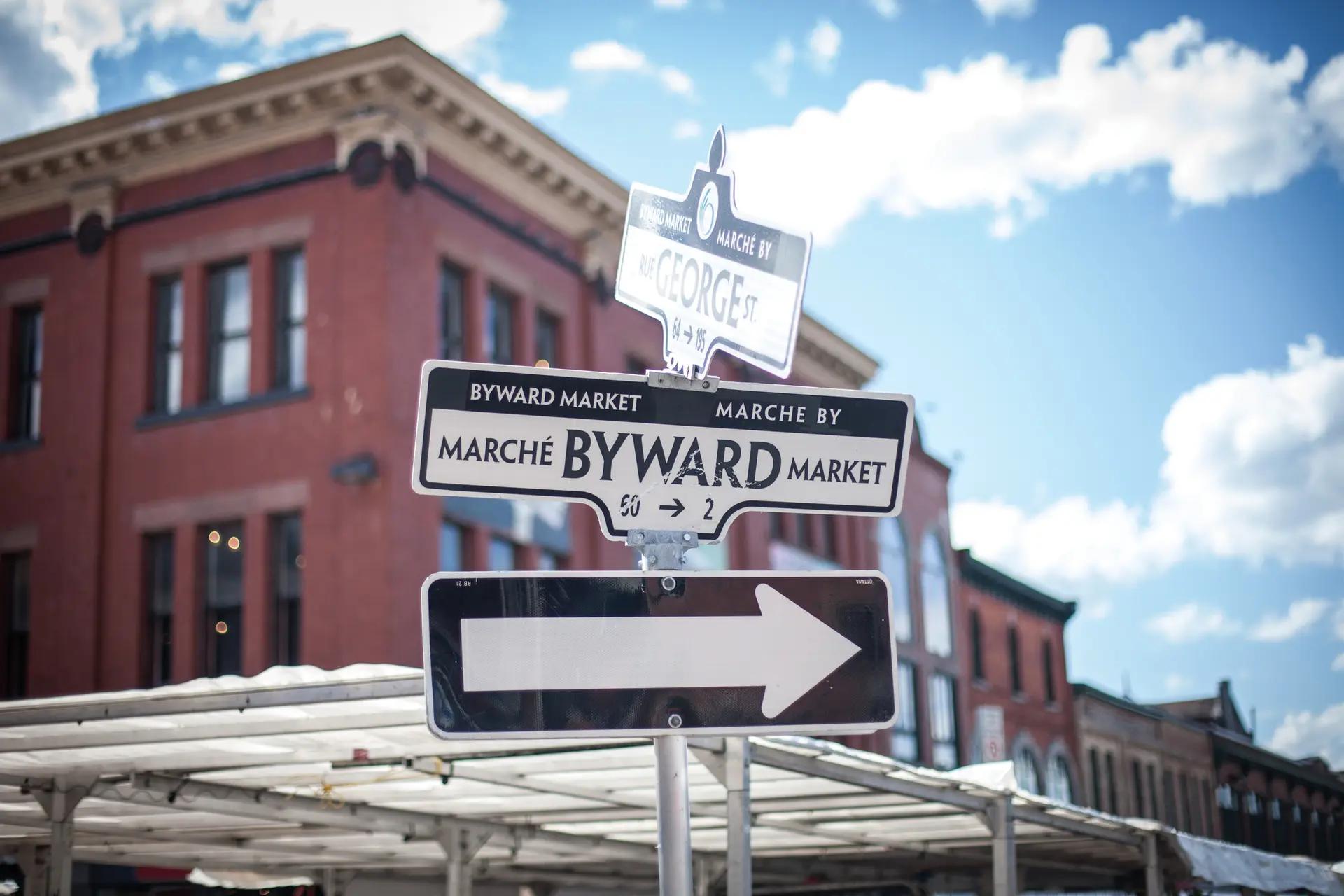 Close-up of a bilingual ByWard Market directional sign in English and French against a bright blue sky in Ottawa