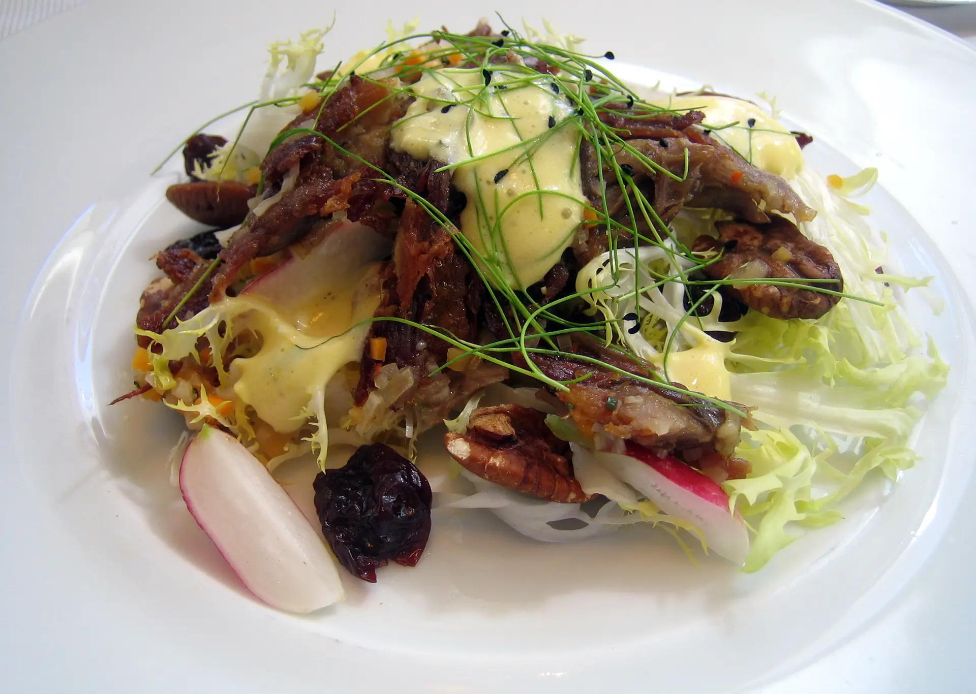 A plated duck confit salad with frisée, radish, pecans, dried cherries, and creamy dressing at an Ottawa restaurant