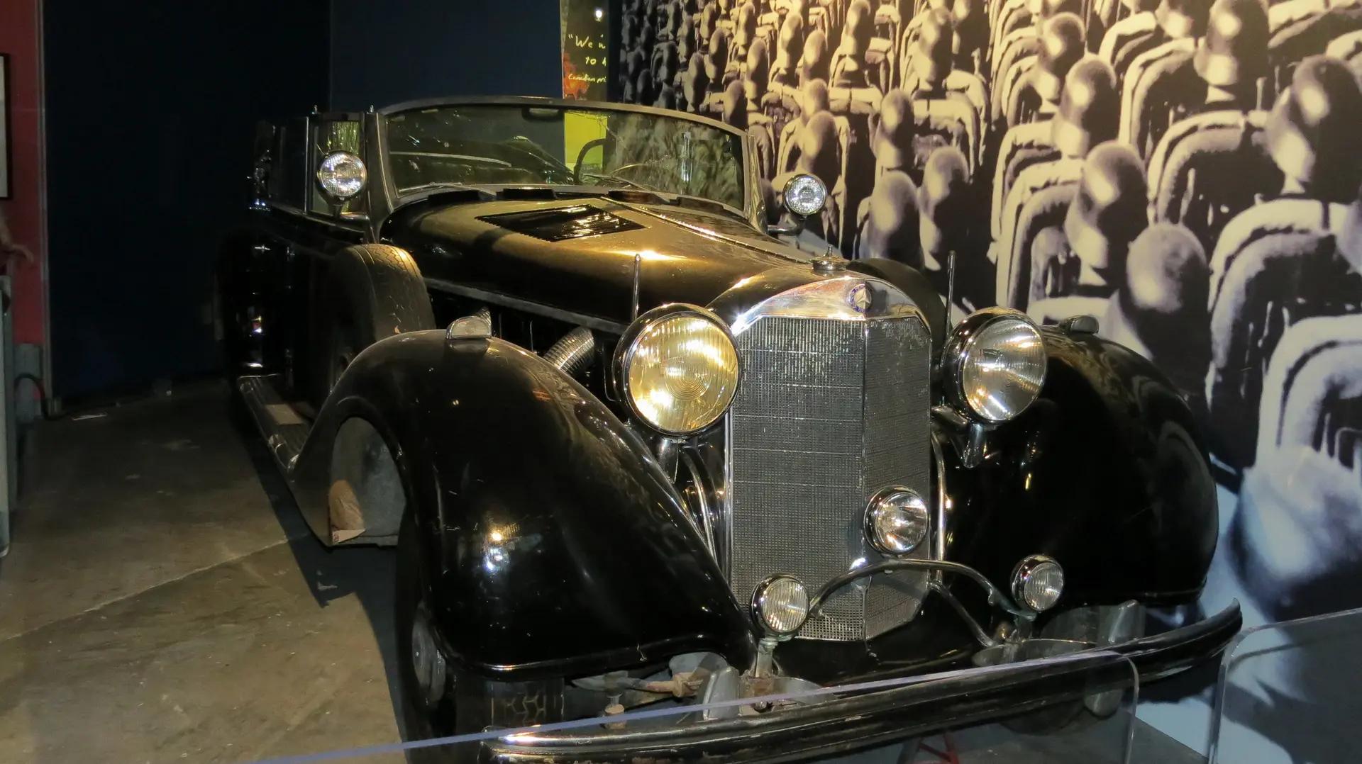 A restored black vintage convertible on display inside Ottawa's Canadian War Museum against a dramatic black and white photo backdrop