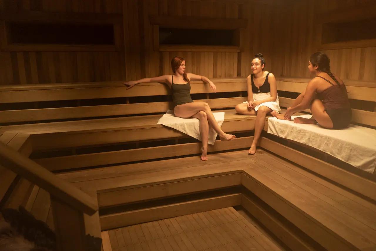 Three women relax and chat inside a warm cedar Finnish sauna at Scandinave Spa Blue Mountain near the Niagara Escarpment.