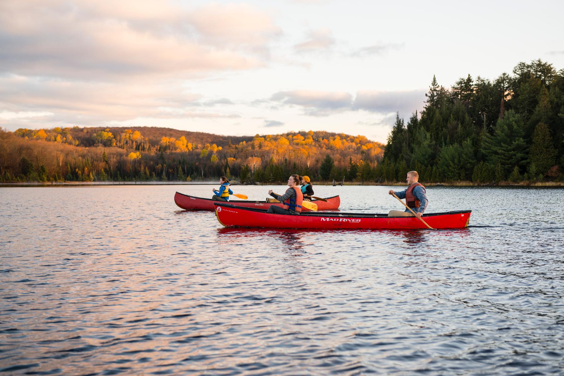 People canoeing on a calm lake surrounded by colourful autumn forest at sunset