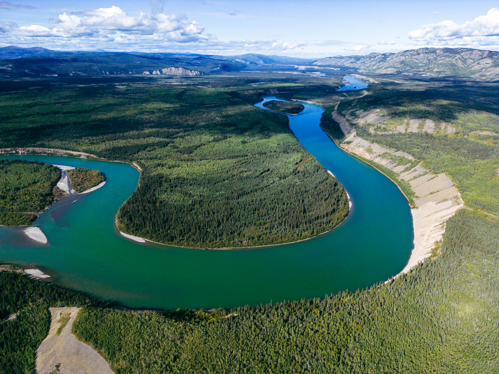 Aerial view of a winding turquoise river flowing through a vast forested valley