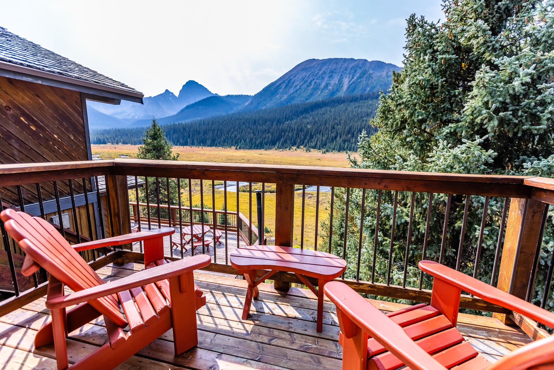Red Muskoka chairs on a lodge deck at Mount Engadine Lodge overlooking Moose Meadows and Rocky Mountain peaks in Spray Valley Provincial Park, Kananaskis Country, Alberta