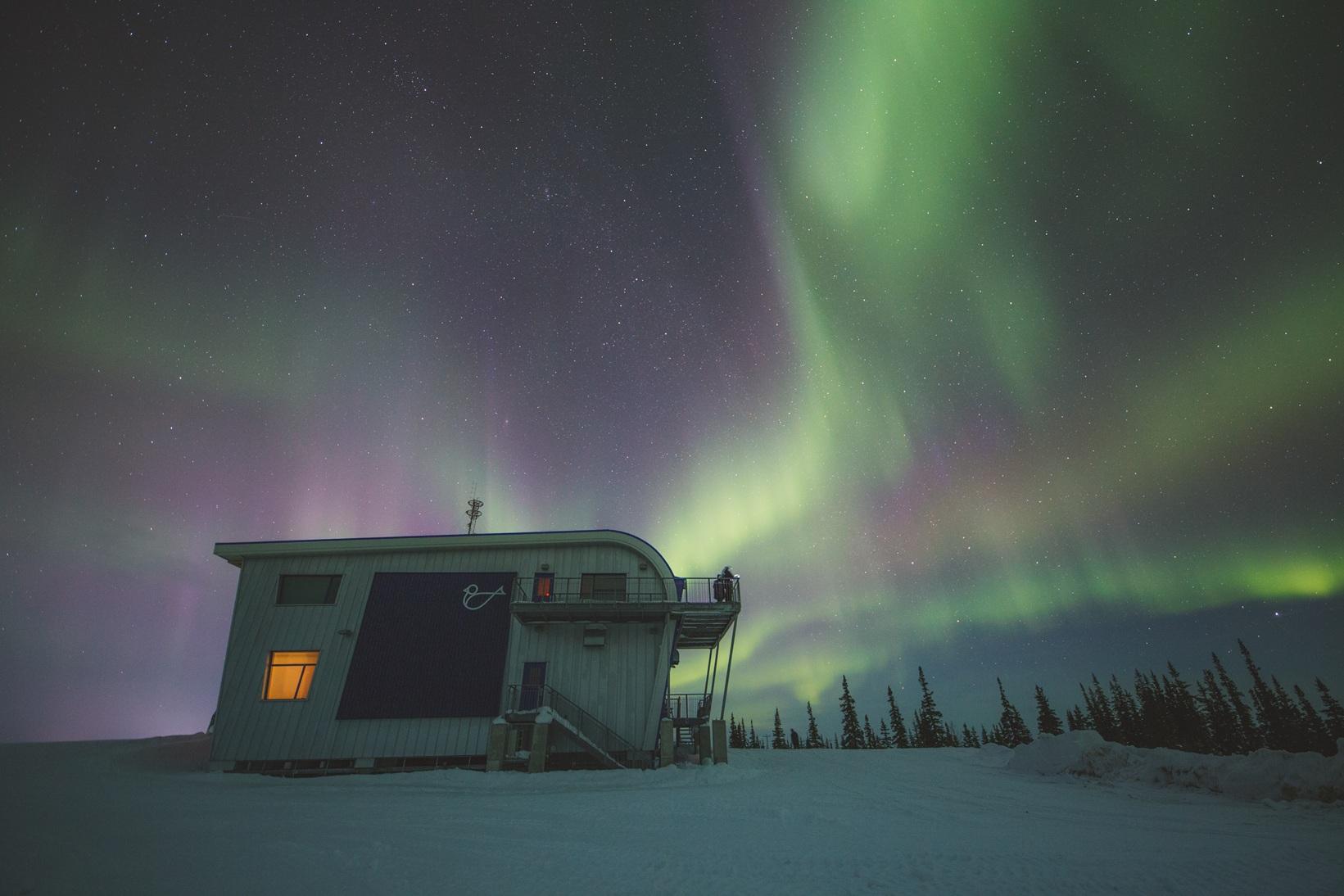 Northern lights glowing above a building in a snowy landscape