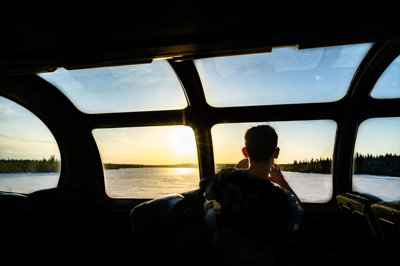 Person looking out a train window at a snowy landscape during sunset