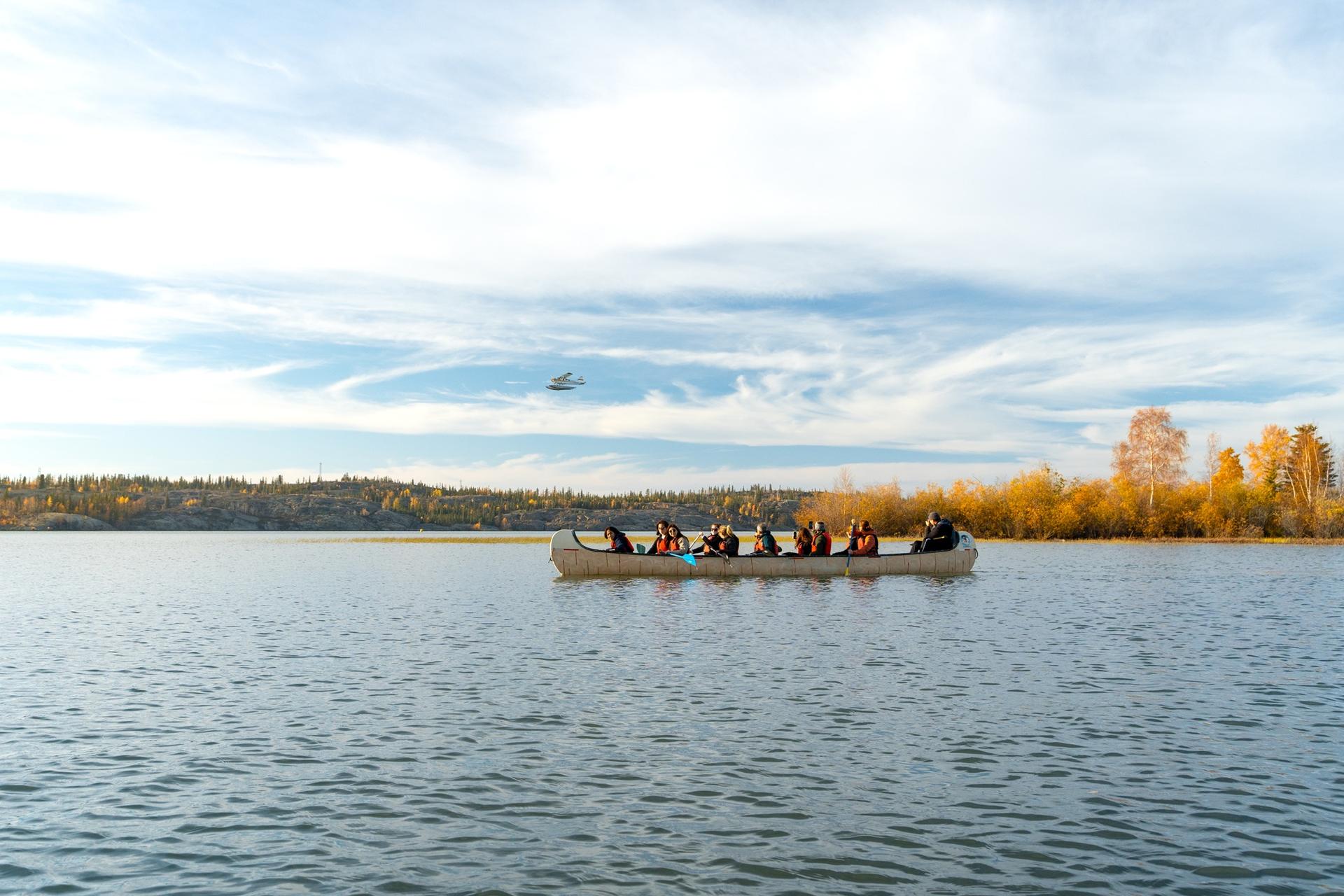 Group paddling a canoe across a calm lake surrounded by autumn foliage
