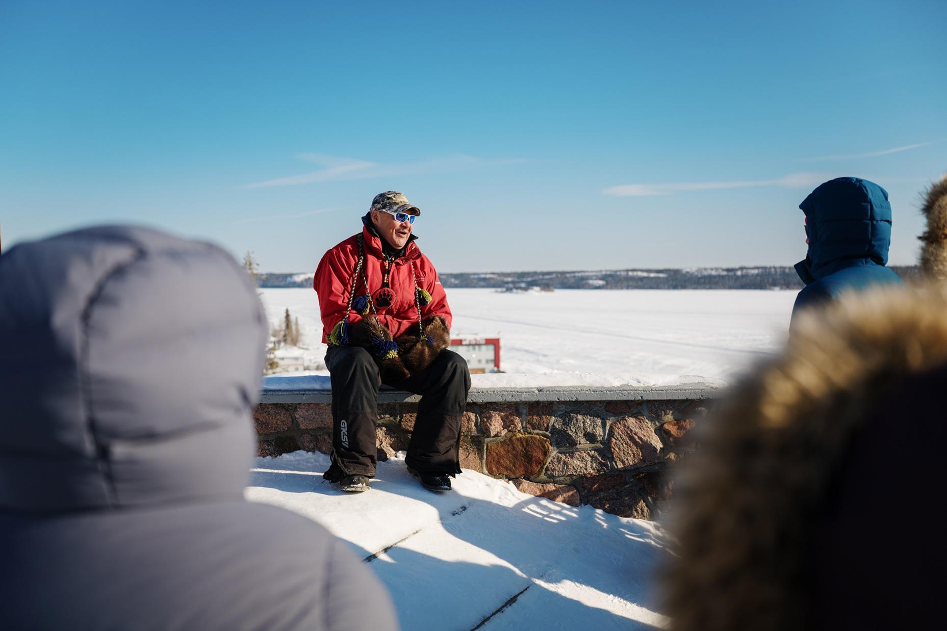 Person speaking to a group beside a frozen lake on a sunny winter day