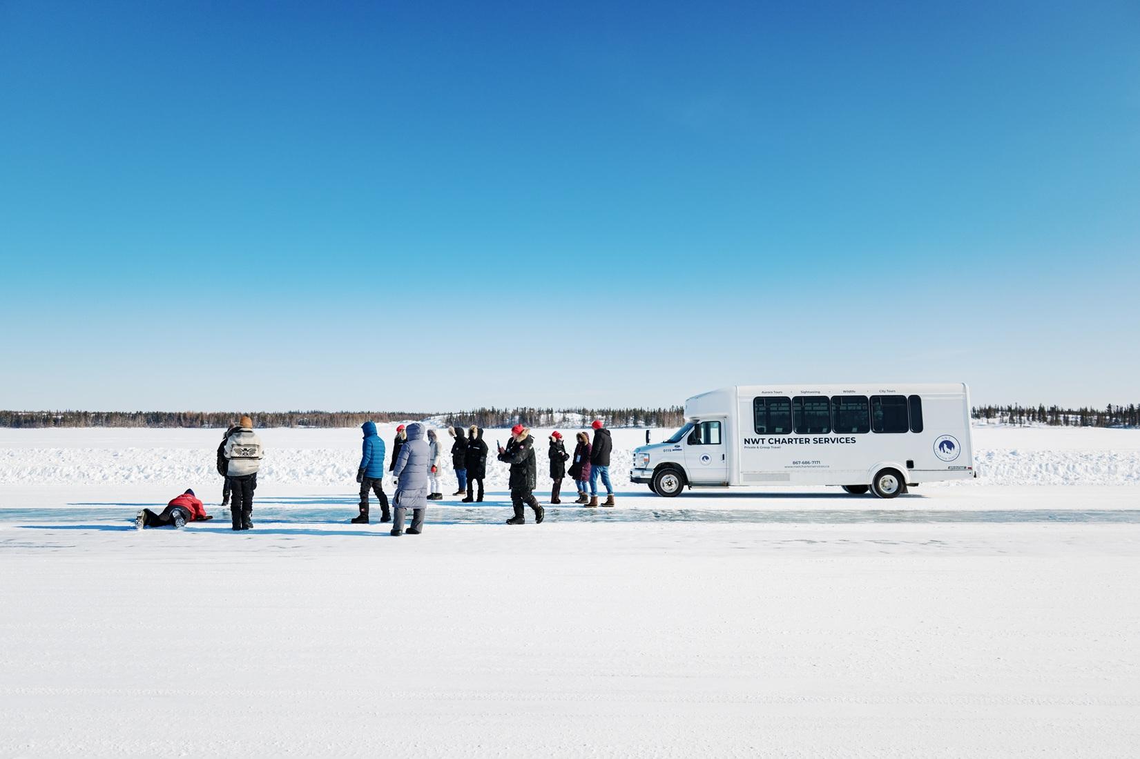 Group gathered beside a tour bus on a frozen lake under a clear blue sky
