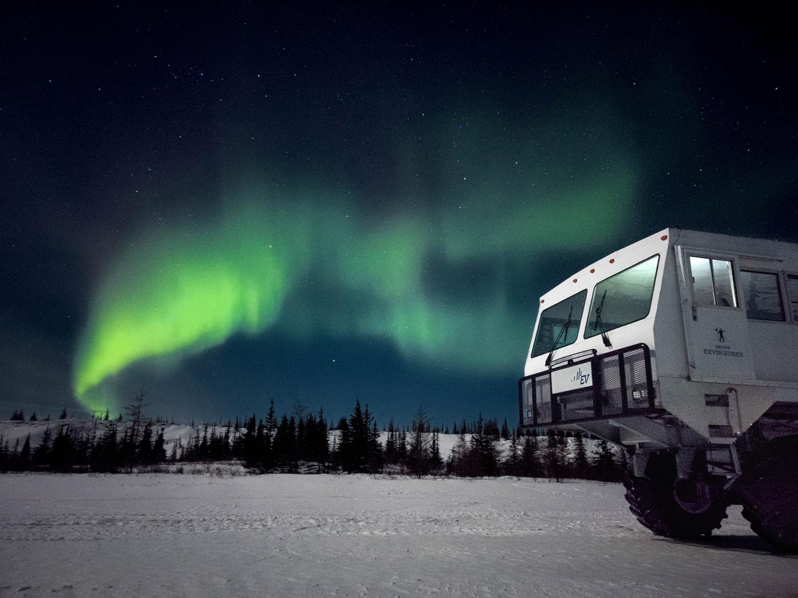 Tundra buggy beneath green northern lights in a snowy landscape
