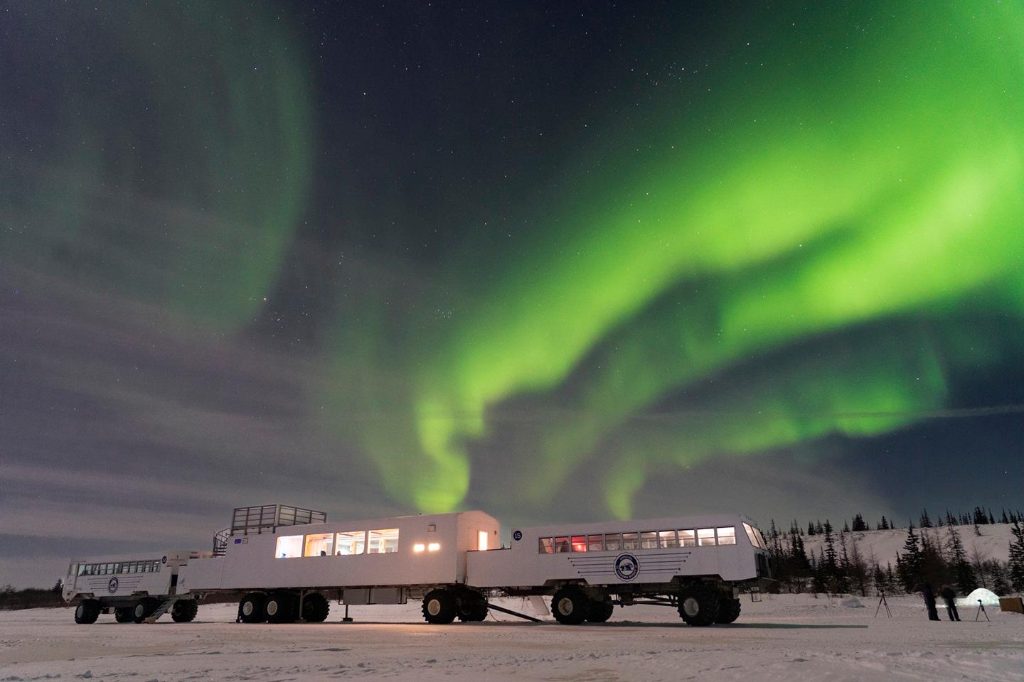 Tundra buggies beneath vivid green northern lights on a snowy landscape