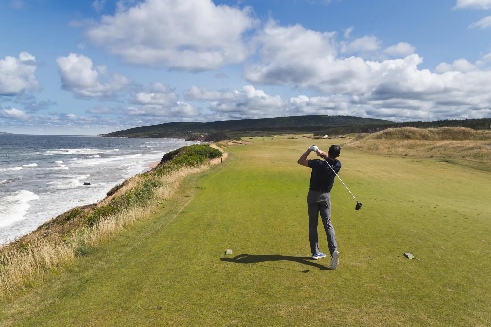 Golfer teeing off at the clifftop Cabot Links course in Inverness, Cape Breton Island, with the Gulf of St. Lawrence below