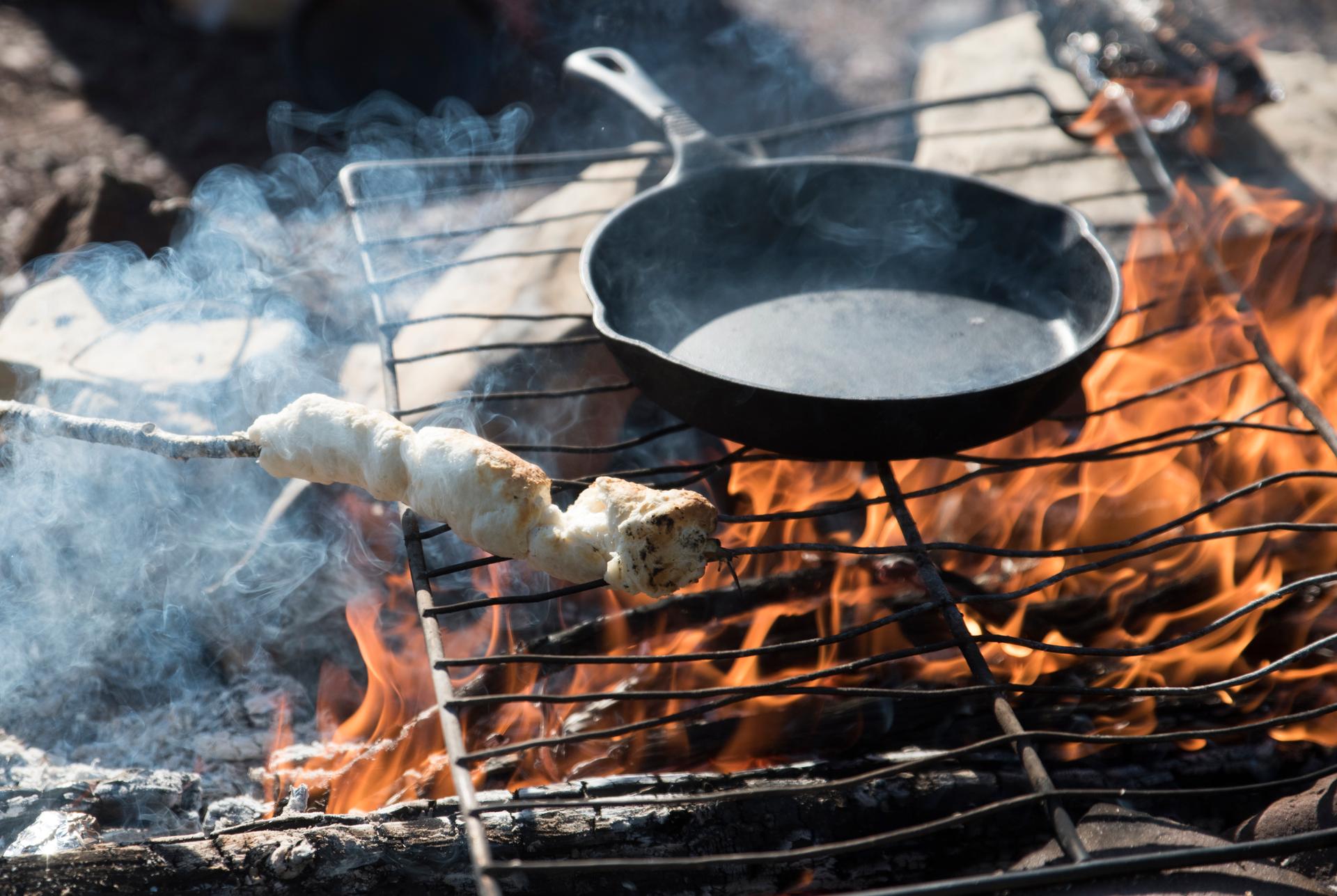 Bannock dough twisted on a stick and a cast iron pan cooking over a campfire grill at a Northwest Territories campsite