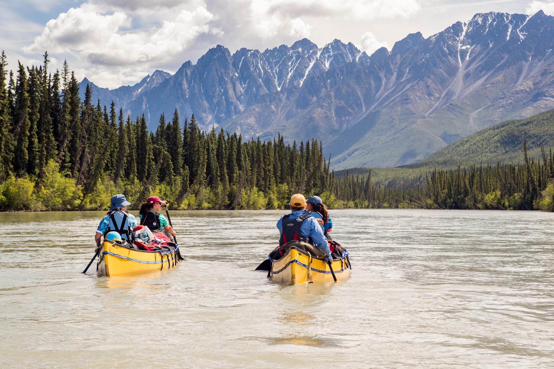 Two canoes with paddlers on a river below the Mackenzie Mountains in the Northwest Territories, Canada