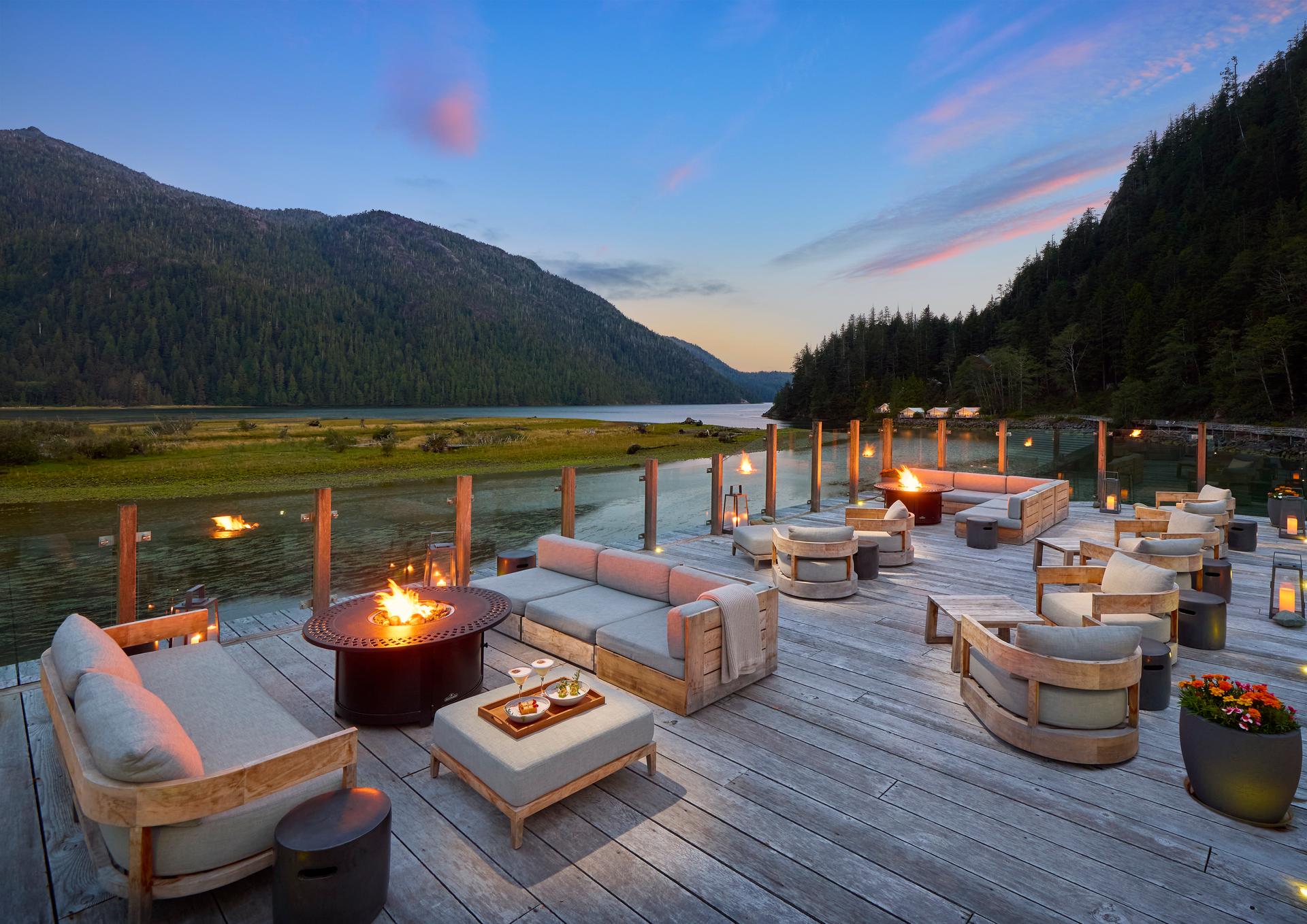 Outdoor lounge deck with fire pits overlooking the river and mountains at dusk at Clayoquot Wilderness Lodge near Tofino, British Columbia