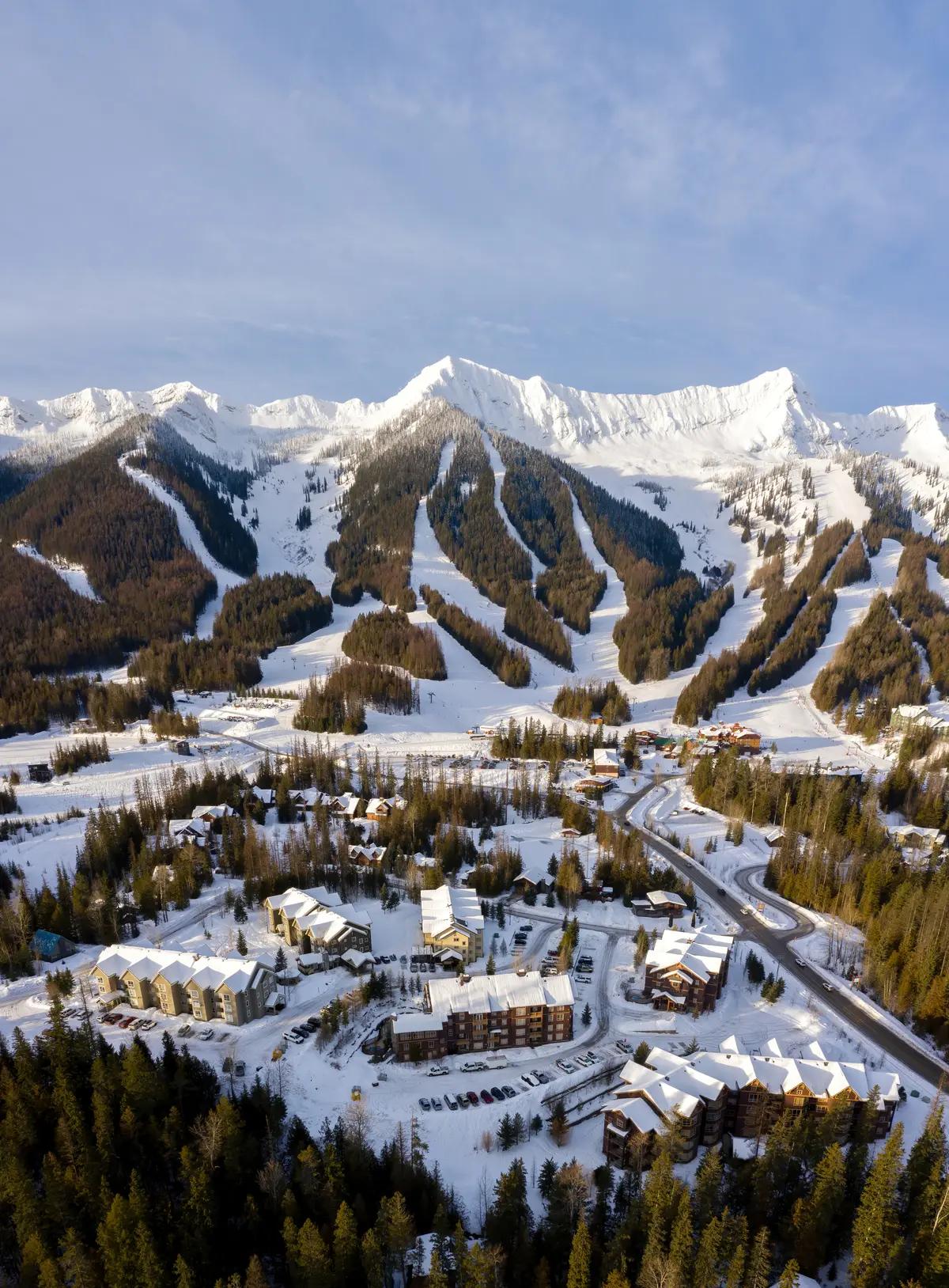 An aerial view of Fernie Alpine Resort's snow-covered village and lodges nestled below dramatic mountain ski runs in British Columbia.