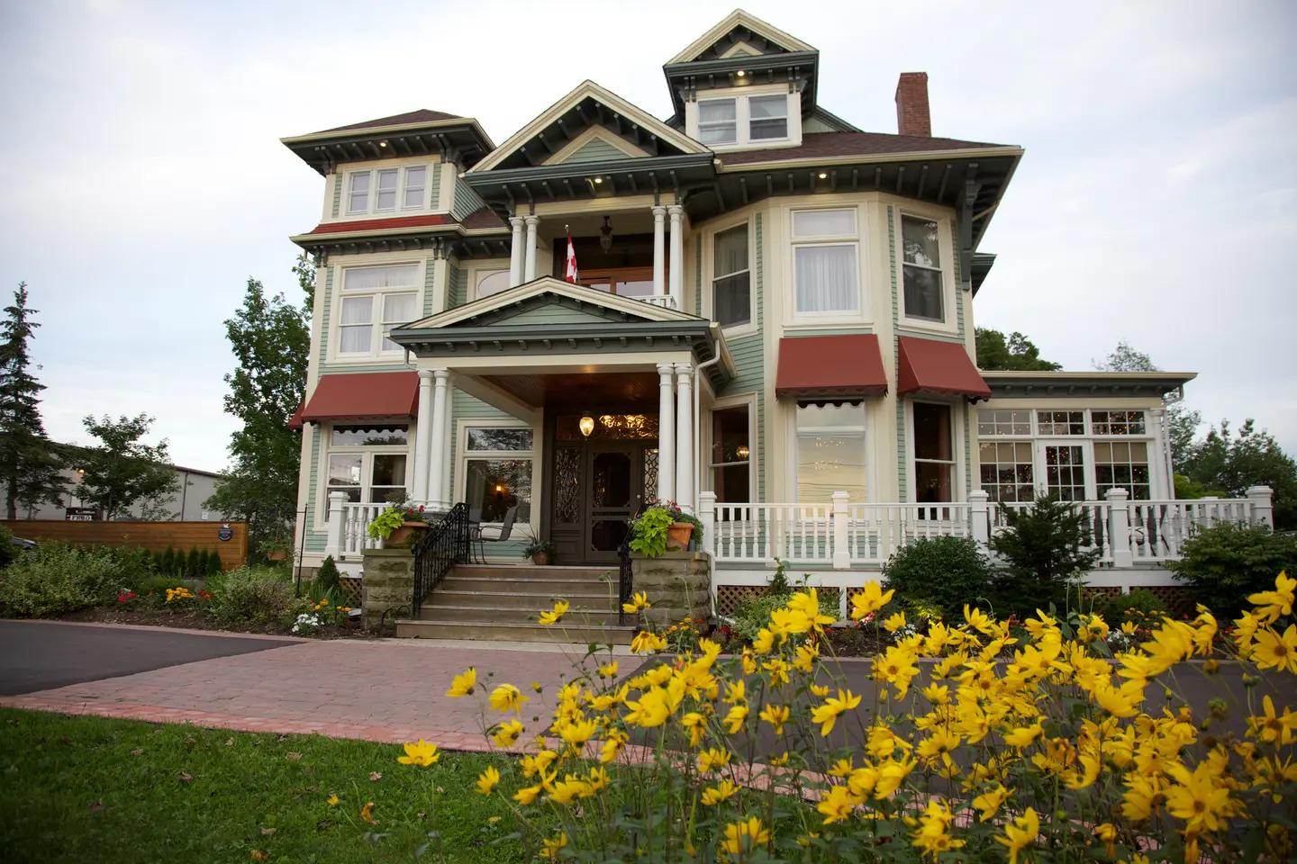 The grand Victorian exterior of Maison Tait House country inn in Shediac, New Brunswick, framed by yellow wildflowers.