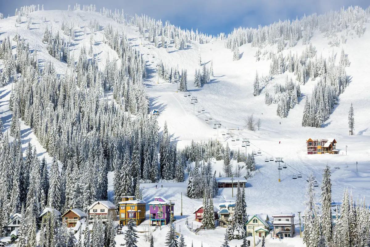 Colorful village buildings and snow-laden evergreens along the base of SilverStar Mountain Resort's wide-open ski runs in Vernon, BC.