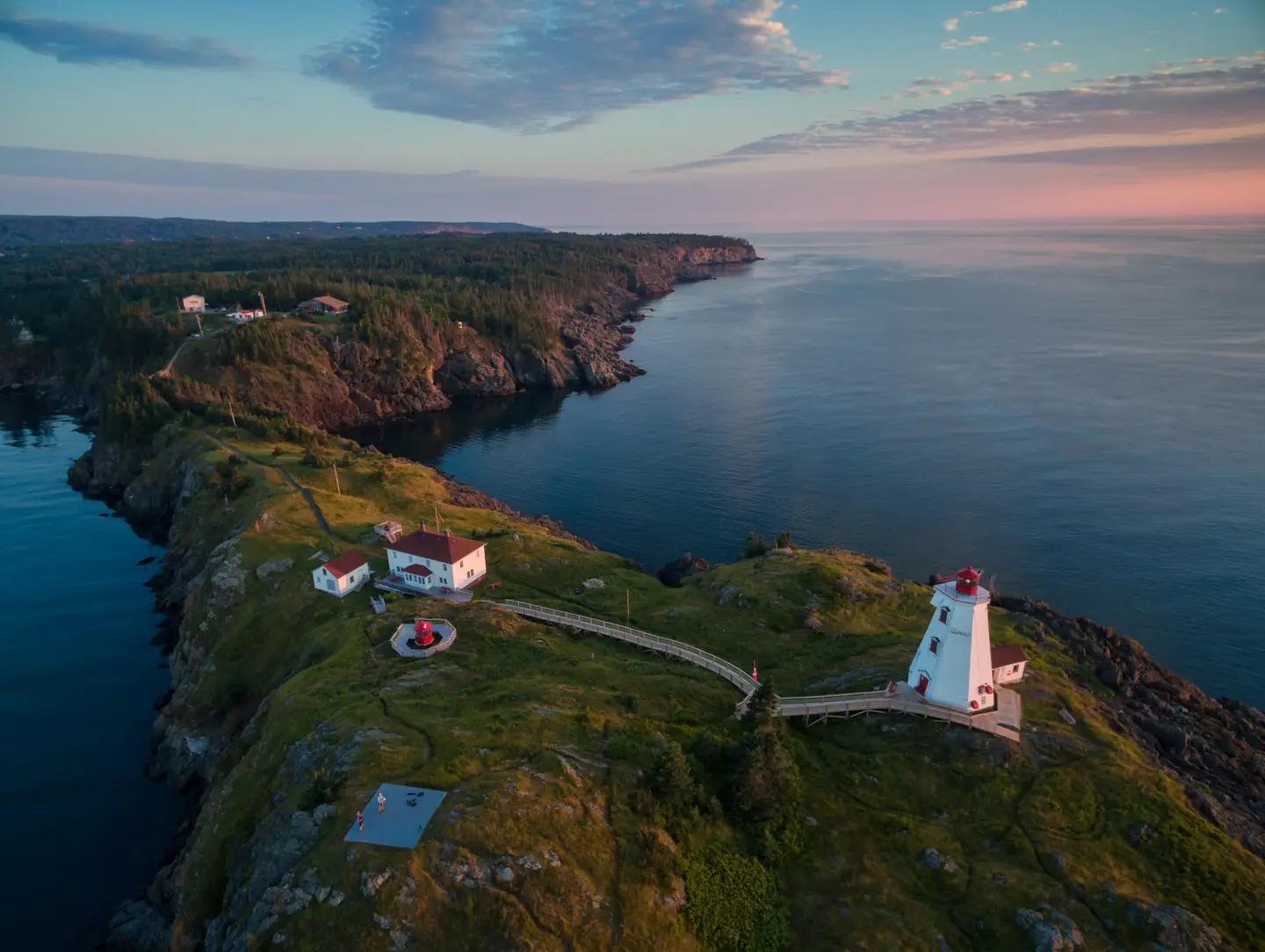 Aerial view of Swallowtail Lighthouse perched on emerald cliffs above the sea at Grand Manan Island, New Brunswick, at sunset.